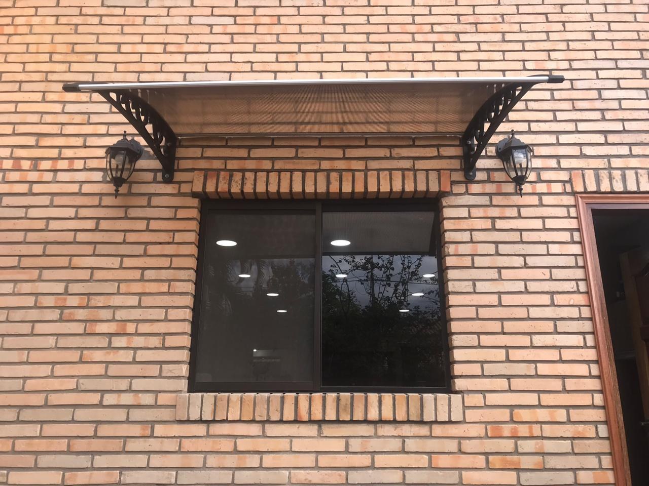 Alero de policarbonato con ménsulas decorativas sobre la ventana de una casa de ladrillo visto · MÁS VIDRIOS