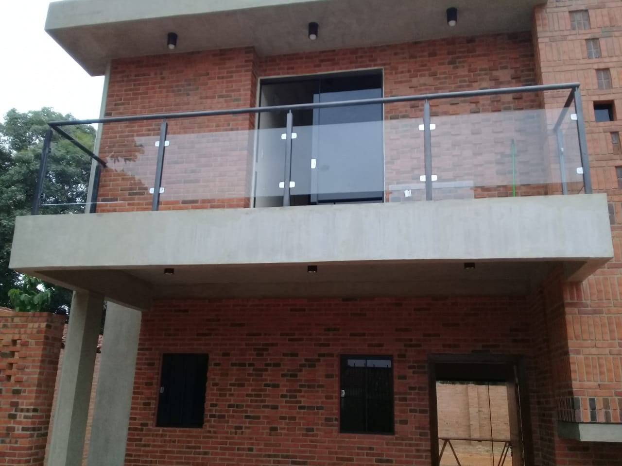 Baranda de vidrio con pasamanos de acero inoxidable en el balcón de una casa de ladrillo visto · MÁS VIDRIOS