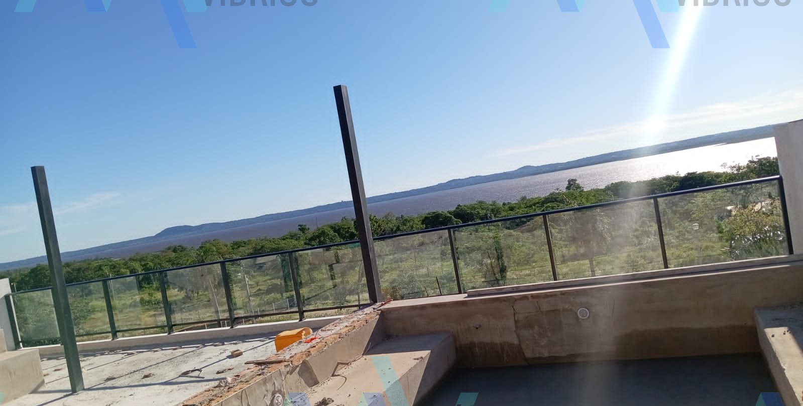 Baranda de vidrio y aluminio negro cerrando una terraza con piscina en obra · MÁS VIDRIOS