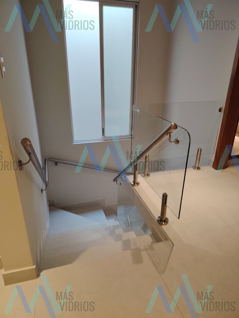 Baranda de vidrio curvo con parantes y pasamanos de acero inoxidable en escalera interior · MÁS VIDRIOS