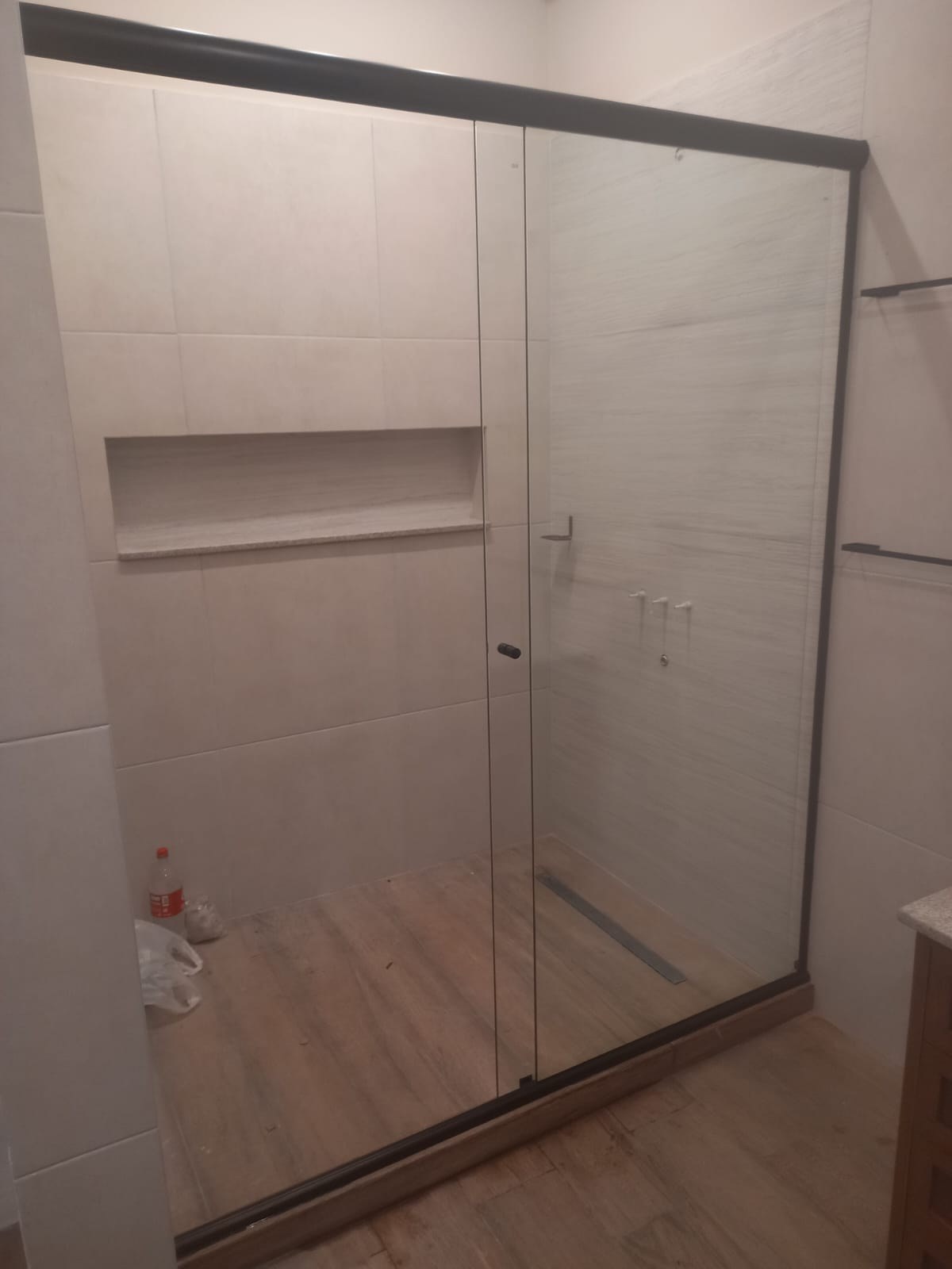 Box de ducha corredizo en vidrio transparente sobre baño con piso símil madera · MÁS VIDRIOS