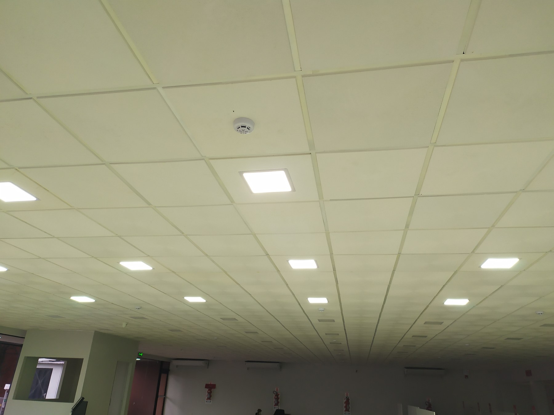 Cielo raso desmontable con luminarias LED encendidas en salón amplio · MÁS VIDRIOS