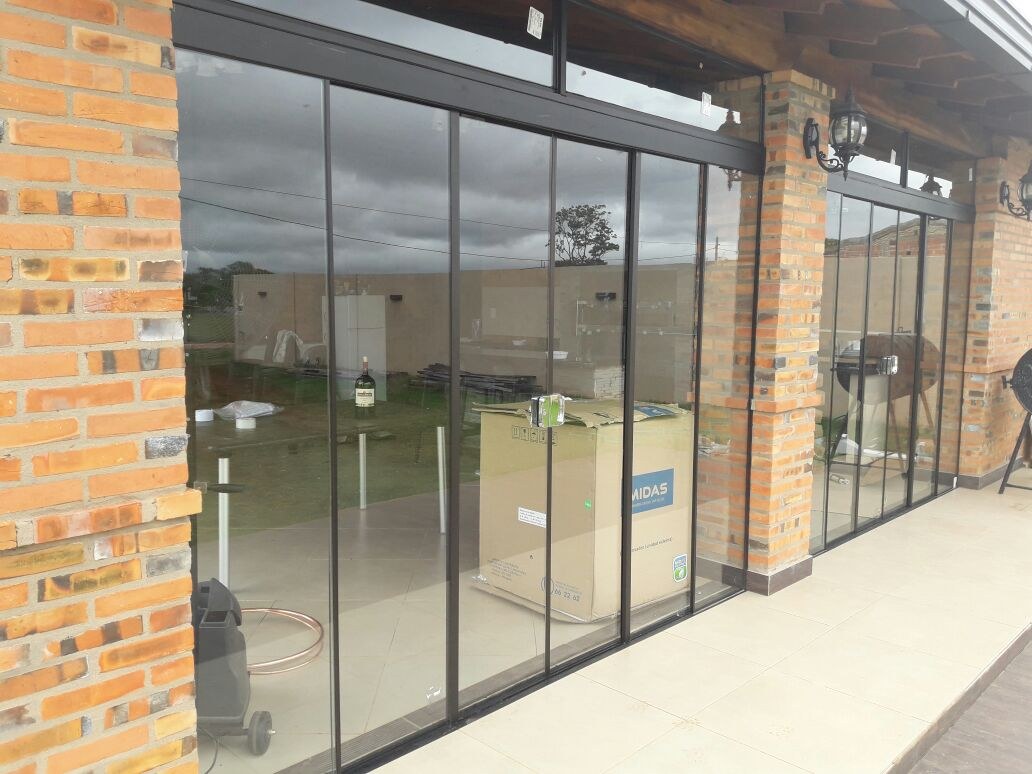 Puertas corredizas de vidrio templado sin marco cerrando una galería entre columnas de ladrillo · MÁS VIDRIOS
