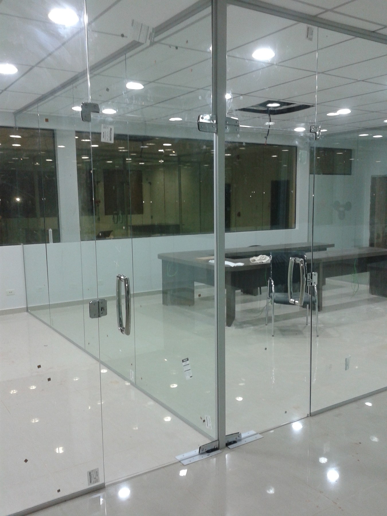 División de oficina en vidrio con puerta batiente y herrajes a la vista · MÁS VIDRIOS