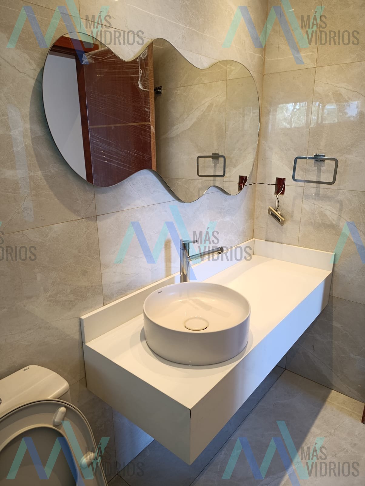 Espejo de diseño orgánico sobre bacha flotante en baño con revestimiento símil mármol · MÁS VIDRIOS