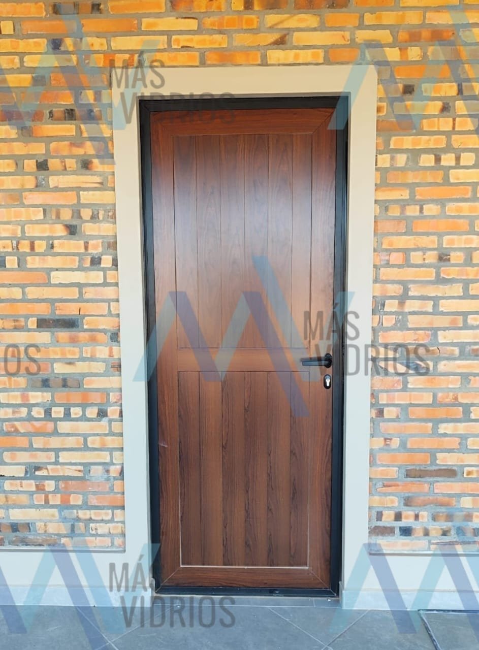Puerta de aluminio símil madera con marco negro en fachada de ladrillo · MÁS VIDRIOS