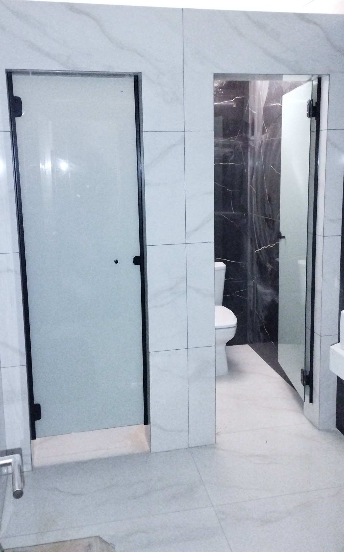 Puerta batiente de vidrio ploteado con herrajes negros en baño de mármol · MÁS VIDRIOS