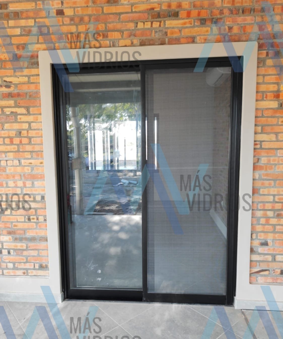 Puerta corrediza de aluminio negro con mosquitero en fachada de ladrillo visto · MÁS VIDRIOS
