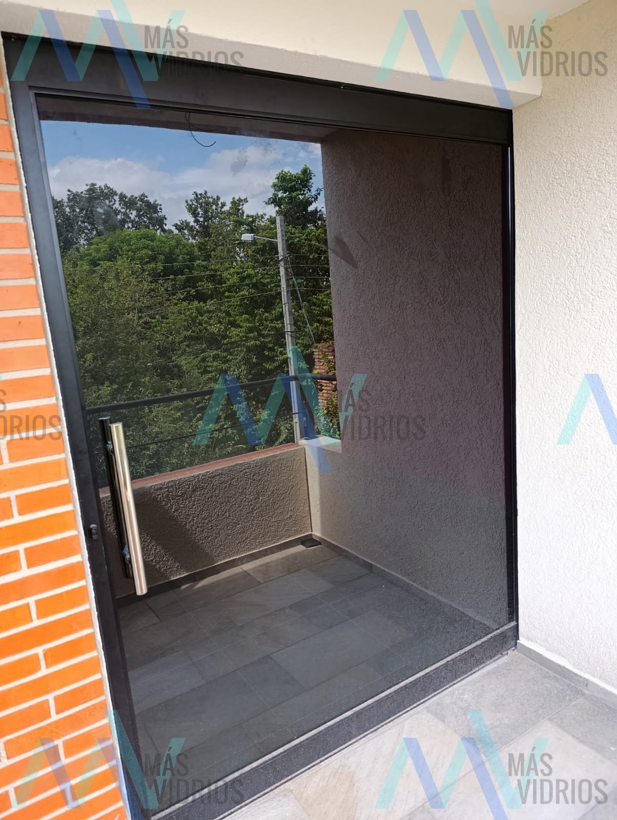 Puerta corrediza de vidrio fumé con barral de acero inoxidable en balcón · MÁS VIDRIOS