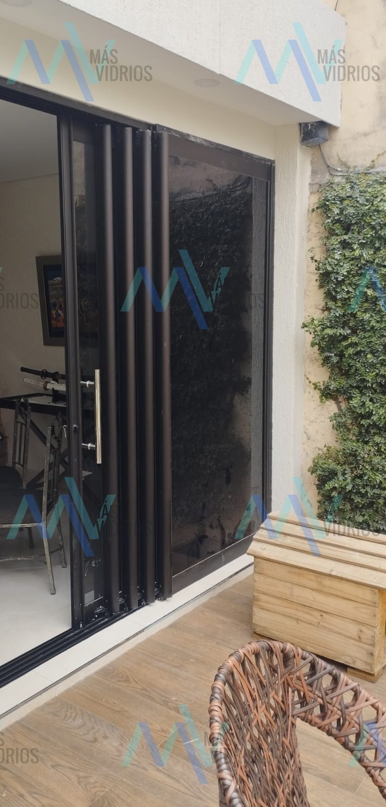 Puerta plegable de vidrio fumé con perfiles de aluminio oscuro en patio residencial · MÁS VIDRIOS