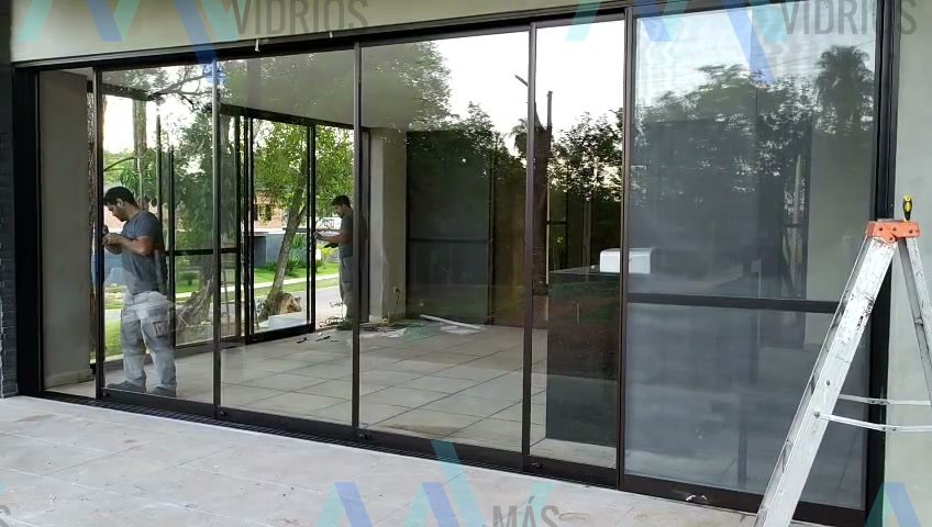 Frente corredizo de aluminio negro y vidrio cerrando la galería de una vivienda · MÁS VIDRIOS