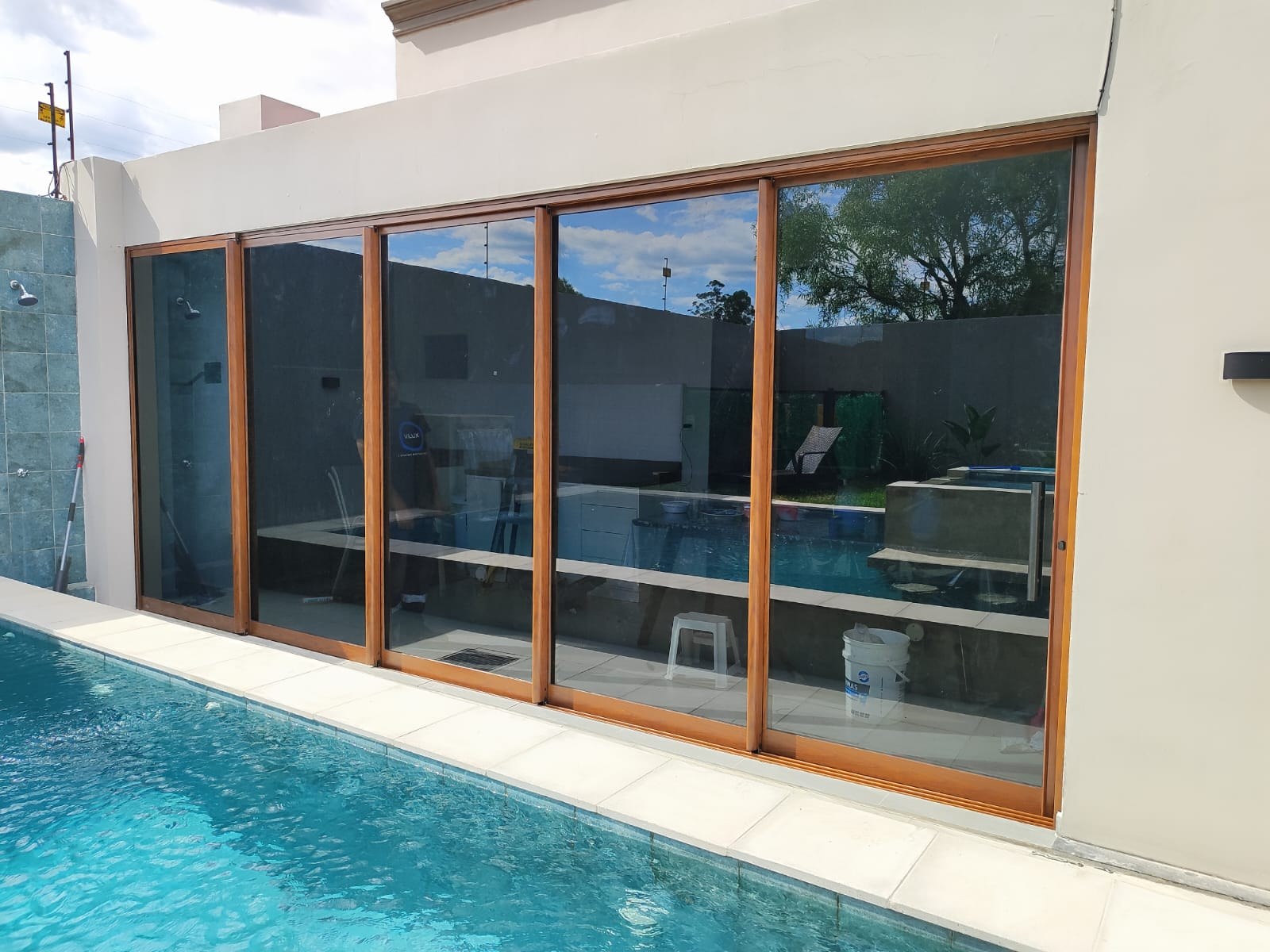 Cerramiento corredizo de aluminio símil madera al borde de la piscina · MÁS VIDRIOS