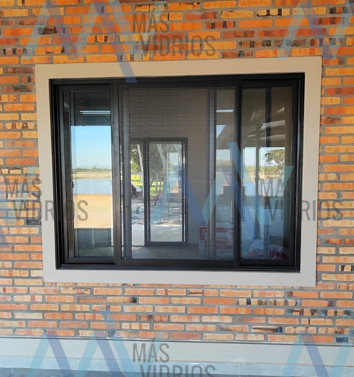 Ventana corrediza de aluminio negro con mosquitero instalada en fachada de ladrillo visto · MÁS VIDRIOS