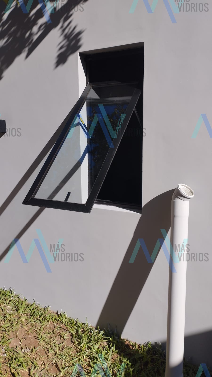 Ventana proyectante de aluminio negro instalada en fachada residencial · MÁS VIDRIOS